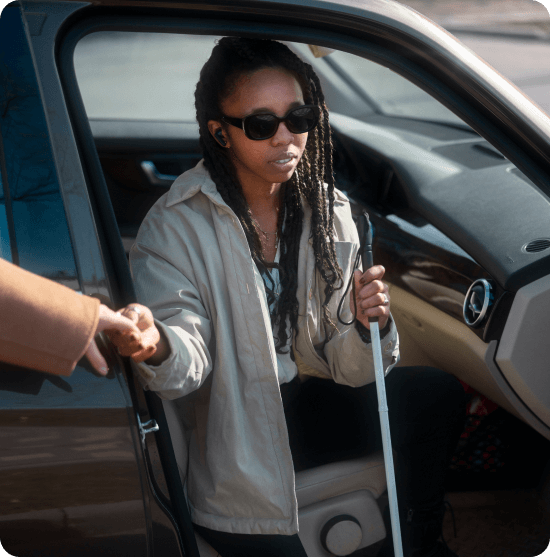 Mujer sordociega bajando de un vehiculo con bastón y gafas.